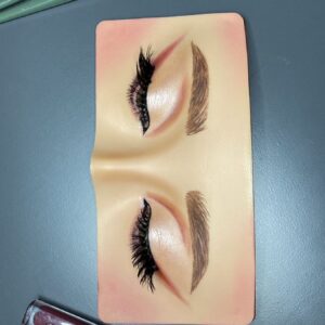 Silicone eye makeup practice board with eyeshadow lashes and brows done, with brushes