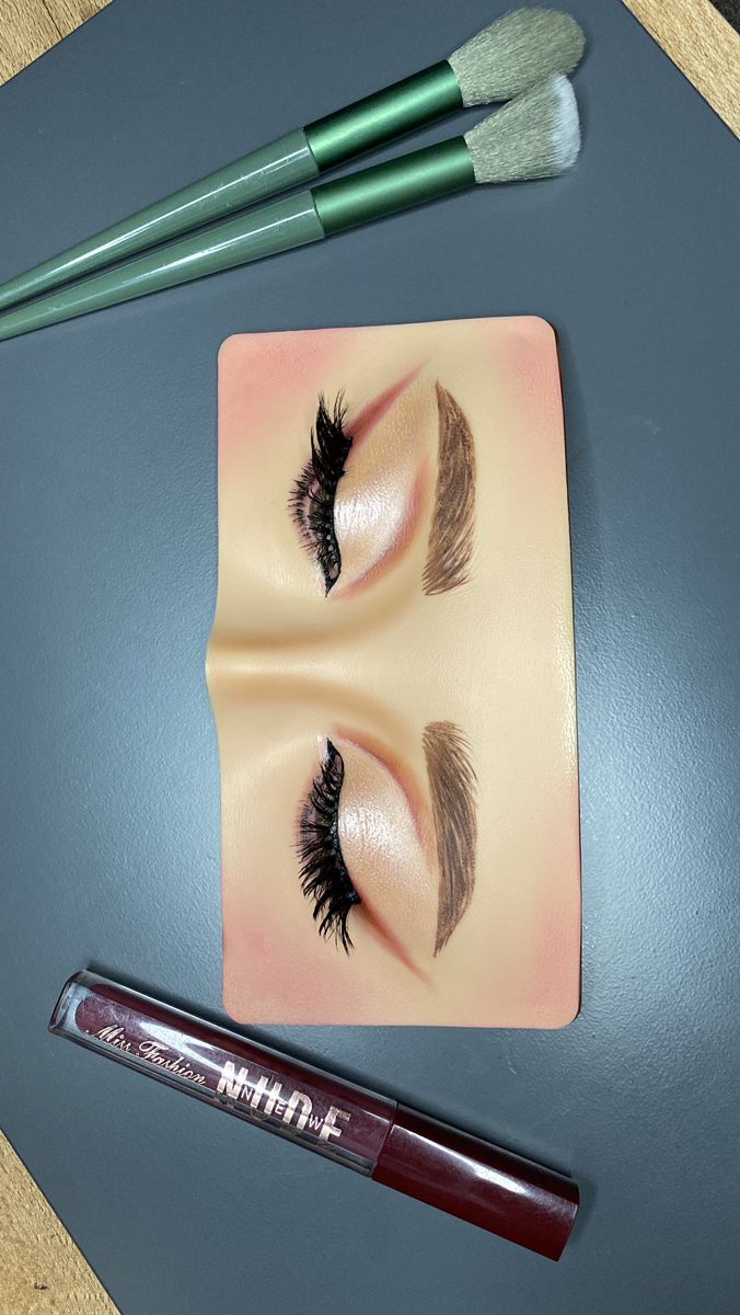 Silicone eye makeup practice board with eyeshadow lashes and brows done, with brushes